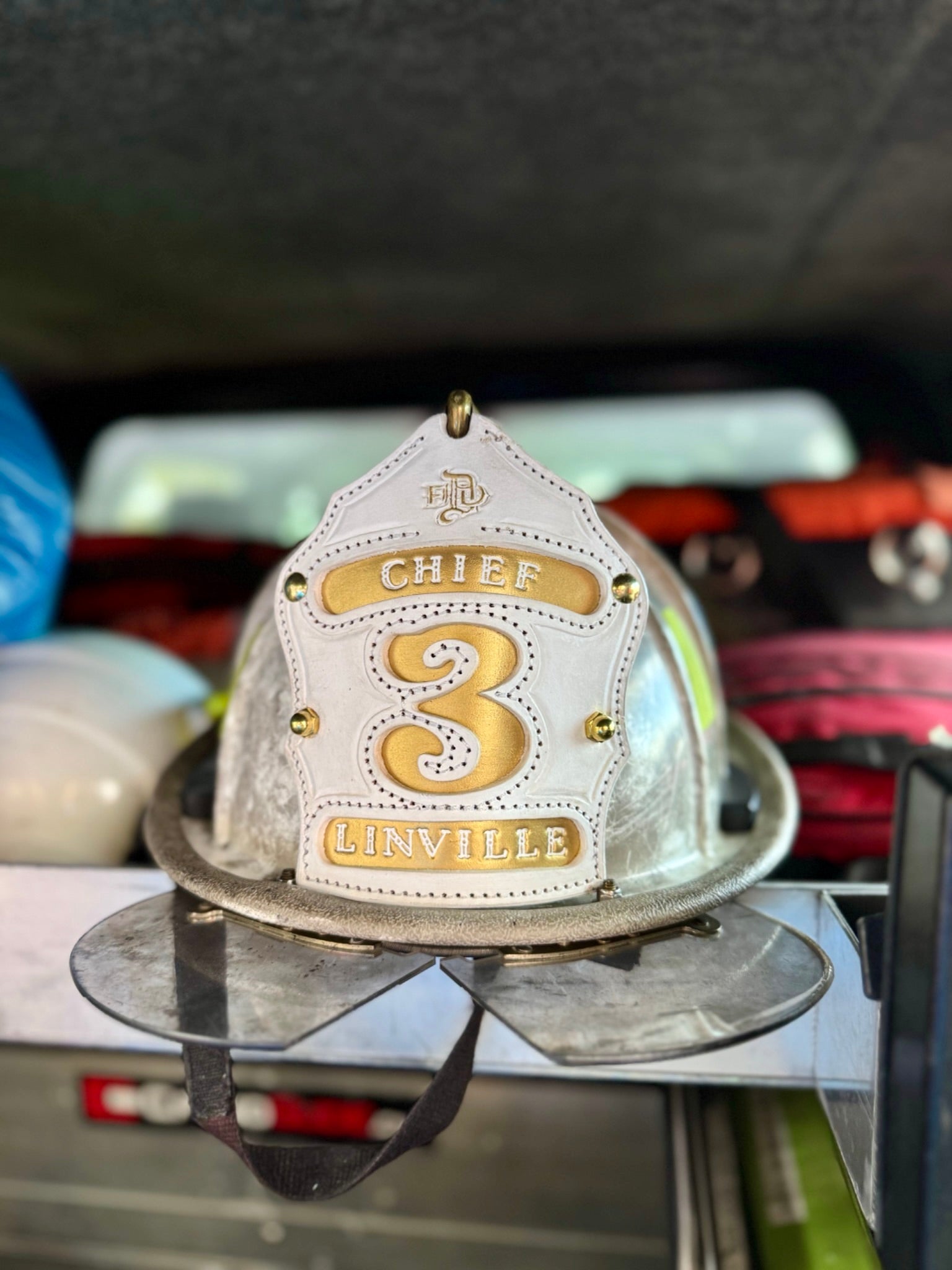 Firefighter helmet with 'Chief 3 Linville' on a stand inside a vehicle.