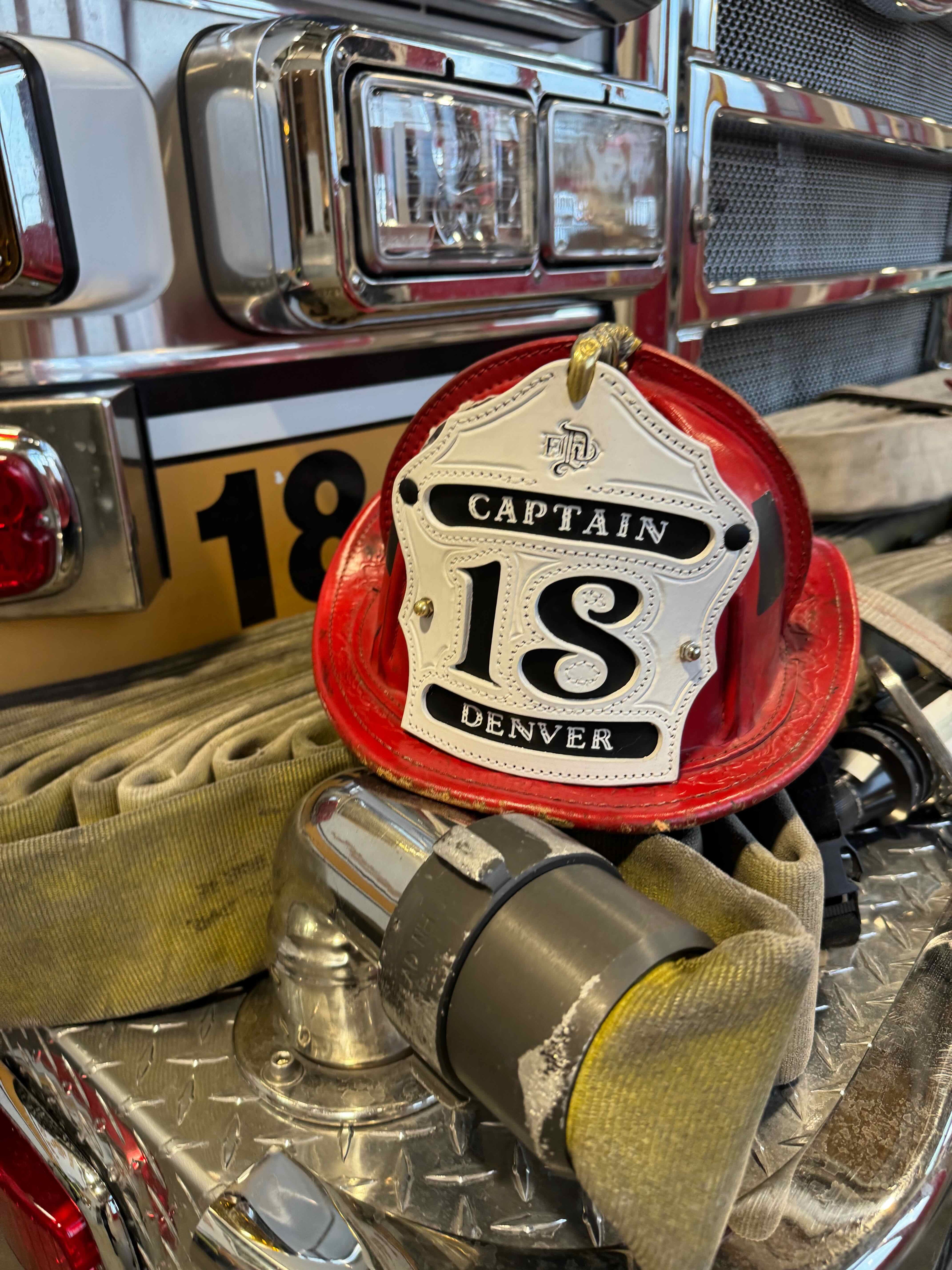 Firefighter helmet with 'Captain 18 Denver' on a fire truck background