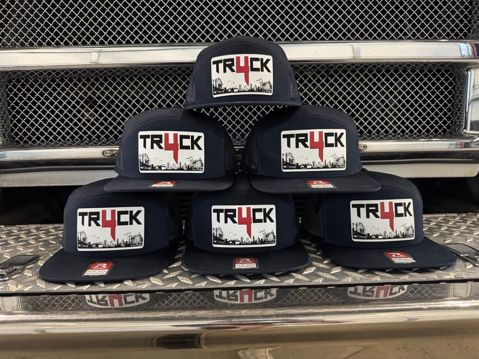 Five black hats with 'TRUCK' logo on a truck bed